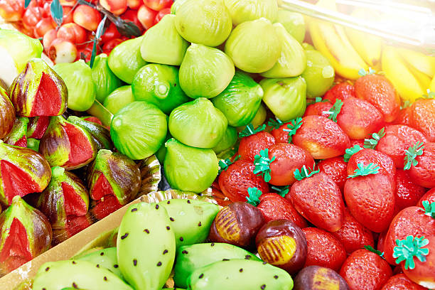 Close up of colorful Thai Look Chup desserts shaped like fruits, made from mung beans and coconut milk, displayed neatly on a wooden tray.