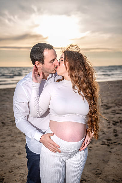 istock Pregnant couple kissing tenderly on sandy beach, sunset casting warm glow while embracing, expressing deep love and anticipation of coming parenthood 2215440571