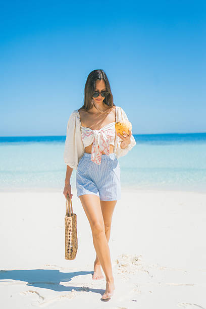 Young woman holds coconut and walks down beach