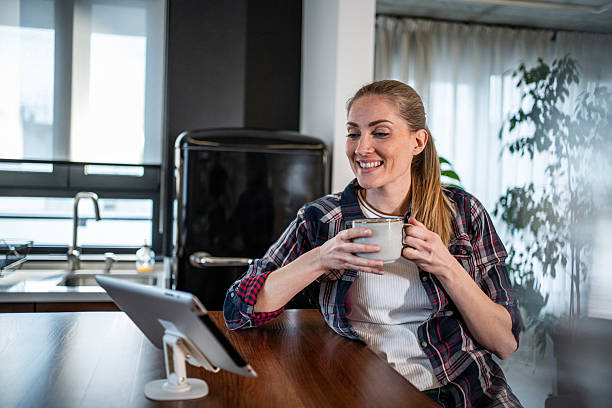 istock Smiling woman enjoying a cup of coffee while video calling on tablet in kitchen 2215444085