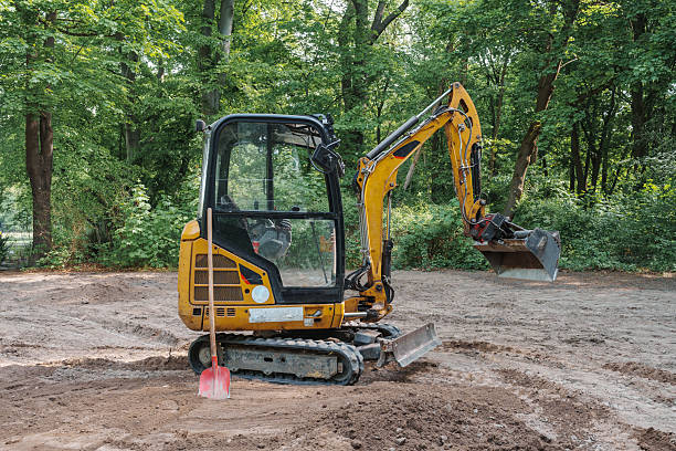 istock A small yellow Crawler excavator with a red shovel leaning against it, parked on a sandy construction site surrounded by green forest trees 2215446095