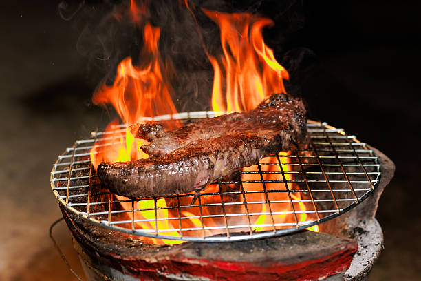 A thick, juicy steak sizzles on a hot grill as flames rise beneath it  capturing the intense heat and flavor of open-fire cooking