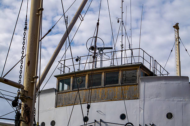 istock section of a historic ship's superstructure with wooden-framed windows, multiple masts, and antennas, set against a partly cloudy sky. The structure highlights technical details and maritime equipment. 2215447328
