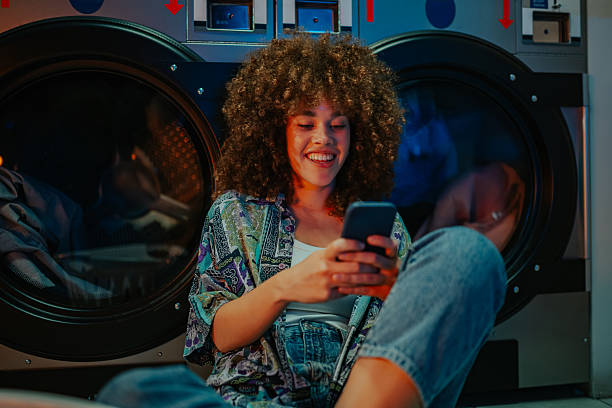istock Young woman using smartphone while waiting at laundromat 2215453727