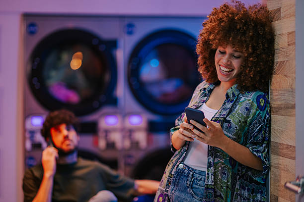 istock Young woman using mobile phone in laundromat while waiting for laundry 2215453776