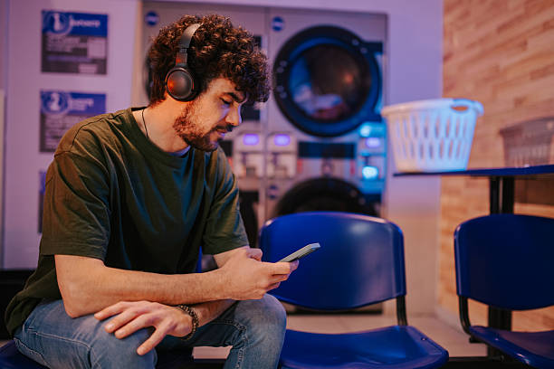 istock Young man listening to music while waiting at laundromat 2215453791