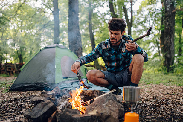 istock Camper adding wood to campfire in forest next to tent 2215455623