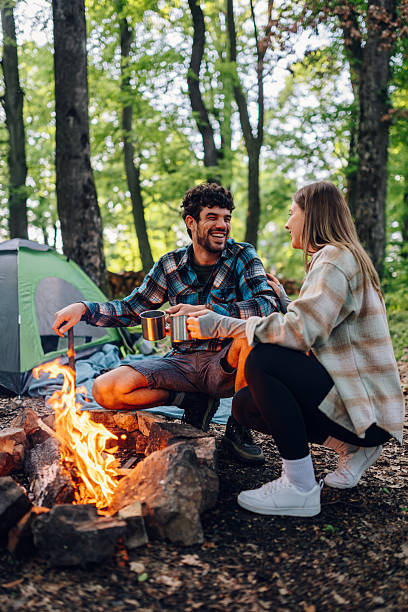 istock Couple camping and drinking coffee by the bonfire in forest 2215455633