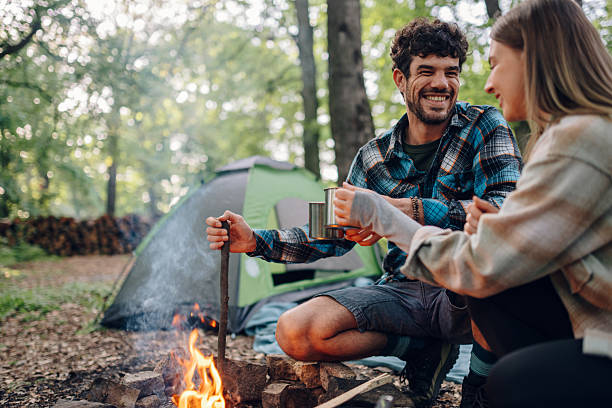 Couple camping and drinking coffee by the bonfire in forest