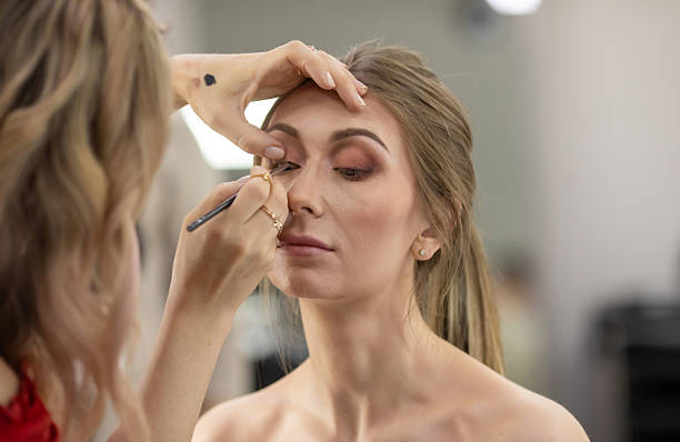 istock Professional beautician applying makeup on beautiful young woman's face. 2215456100