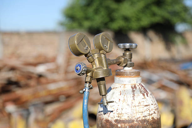The image shows a pressurized oxygen cylinder with a mounted pressure regulator that has two pressure gauges. The gauges are used to measure the gas pressure — one shows the oxygen pressure inside the cylinder, while the other shows the working oxygen pressure coming out of the regulator.This type of equipment is commonly used in welding, medicine, and industry where precise oxygen dosing is important. The background of the image is blurry and indistinct, which further highlights the technical details in the foreground.