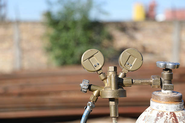 The image shows a pressurized oxygen cylinder with a mounted pressure regulator that has two pressure gauges. The gauges are used to measure the gas pressure — one shows the oxygen pressure inside the cylinder, while the other shows the working oxygen pressure coming out of the regulator.This type of equipment is commonly used in welding, medicine, and industry where precise oxygen dosing is important. The background of the image is blurry and indistinct, which further highlights the technical details in the foreground.