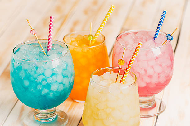 istock Several glasses filled with ice and assorted colorful flavored sodas, with drinking straws, on a white wooden table, close-up. 2215465825