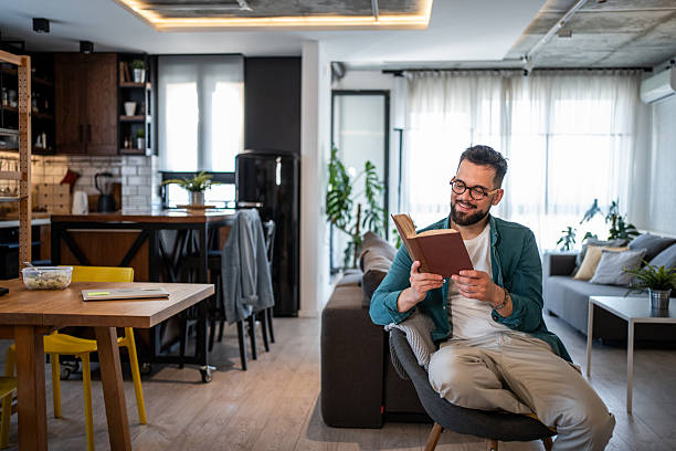 istock Young man reading a book in his modern apartment 2215476745