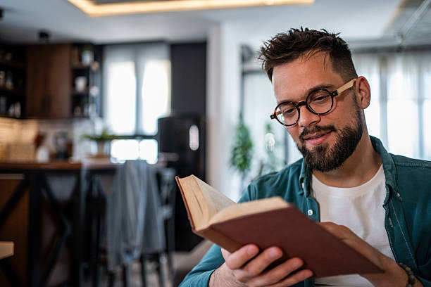 istock Young man reading a book at home in his modern apartment 2215476785