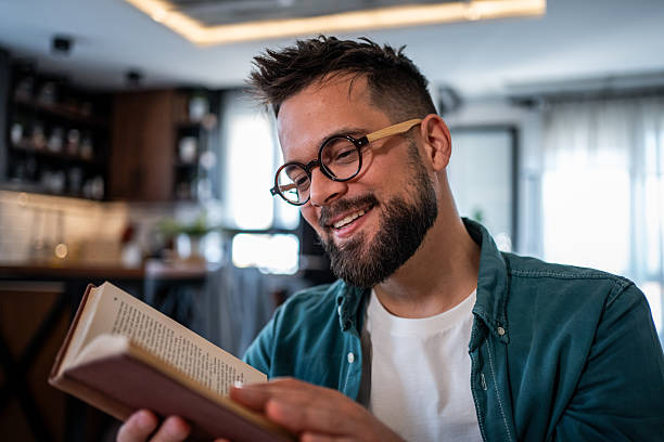 istock Young man smiling and reading a book at home 2215476795
