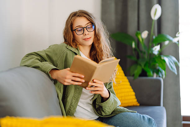 istock Smiling woman with a book enjoying reading while sitting on a sofa in a cozy room. 2215479424