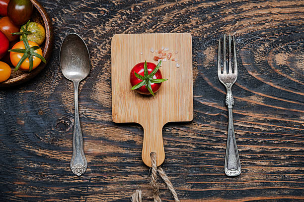 one ripe cherry tomatoes on cutting board.Fork and knife on dark wooden table. view from above.