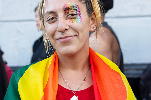 A gay female smiles confidently with a rainbow flag and colorful face paint at a lively pride celebration.