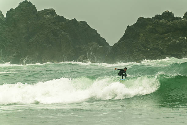 istock Surfer riding a wave near rocky coastline on a cloudy morning 2215483968
