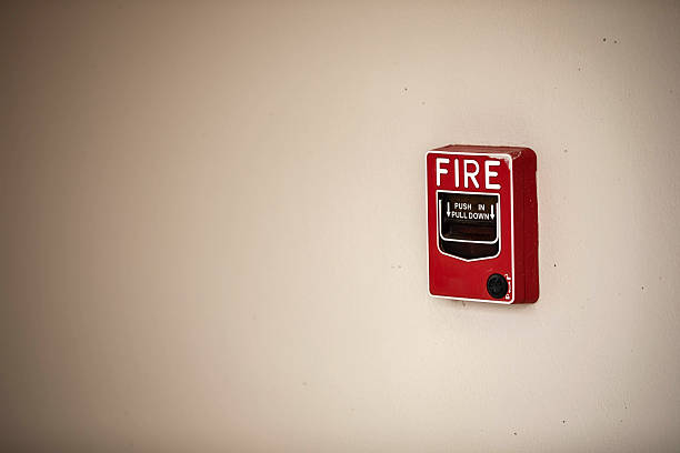 Close-up of a red fire alarm pull station mounted on a beige wall, emphasizing emergency preparedness and safety awareness. Ideal for safety equipment, fire prevention, and building security themes.