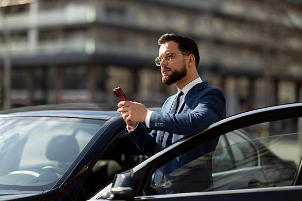 istock Businessman Checking Smartphone Beside CarDescription: 2215487286