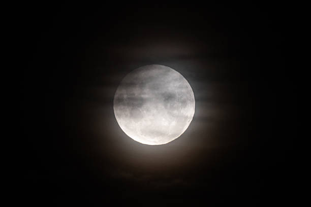 istock A photo of the moon during a partial eclipse, with its top edge slightly darkened and a soft haze from thin clouds diffusing the light 2215487324