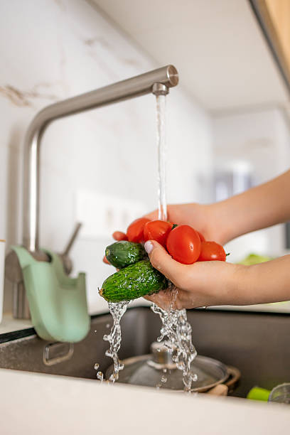 istock Hands rinsing vegetables, including cucumbers and tomatoes, under running water in a home kitchen. 2215488425