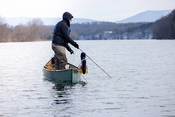 A musky fisherman standing in a canoe on the Shenandoah River in winter