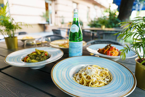 An outdoor table set with colorful Italian pasta dishes and a bottle of sparkling water, creating a fresh and inviting Mediterranean dining atmosphere.