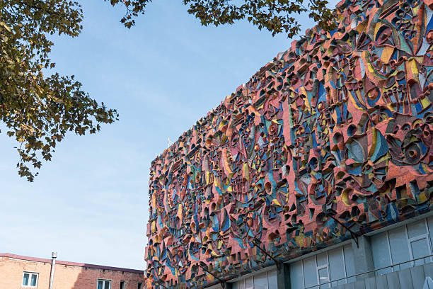 Tbilisi, Georgia - October 31, 2024:  striking view of a building in Tbilisi, Georgia, featuring a large and colorful mosaic facade. The intricate artwork covers a significant portion of the building's exterior, showcasing a variety of shapes and hues. The lower part of the building appears to house a TBC Bank branch. A tree with autumn-toned leaves frames the upper left corner of the image, contrasting with the modern artistic expression on the building.