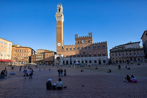 Tourists visiting Piazza del Campo on an autumn morning, Siena, Italy. Torre del Mangia and Palazzo Pubblico in the background.