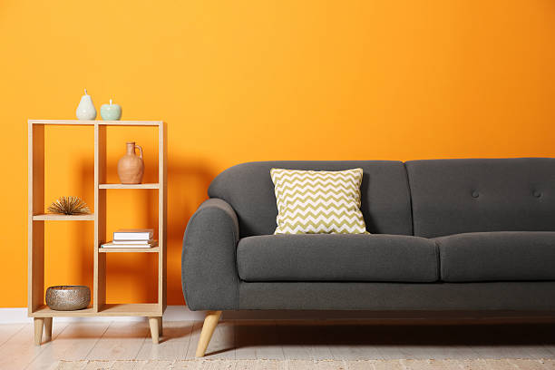 istock Stylish sofa with cushion and decor elements near orange wall 2215514548