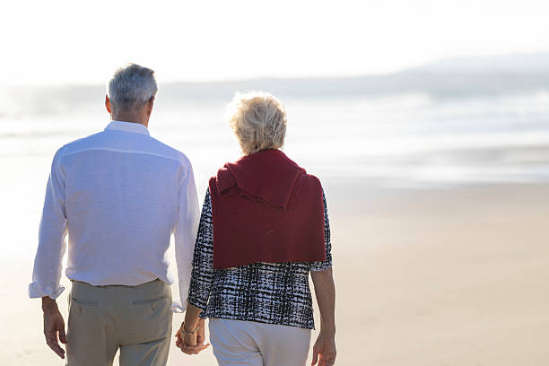 istock Elderly couple holding hands walking on the beach at sunset 2215518751
