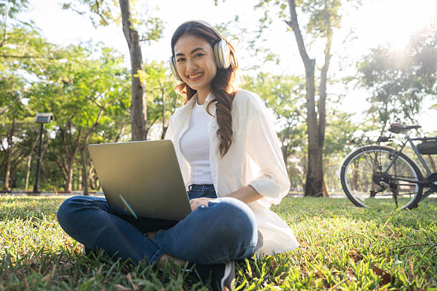 istock Young asian teenager learning with laptop sitting in the public park. Summer time spring young women working outdoors living in nature. Human and nature together 2215524708