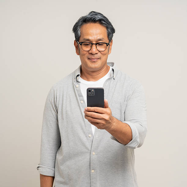istock Handsome asian mature old man standing using smartphone on isolated white background. Happy Portrait of cheerful smiling senior asian man holding cell phone. Mature People and lifestyle 2215525361