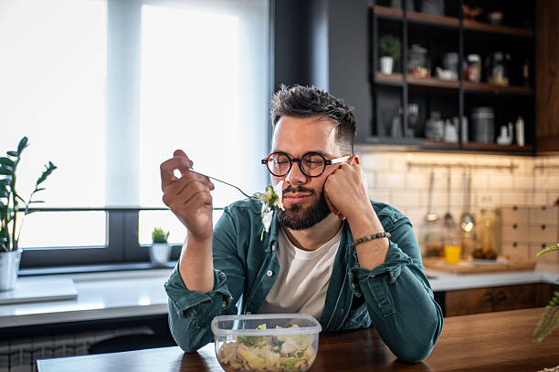 istock Bored young man reluctantly eating salad at home 2215526809