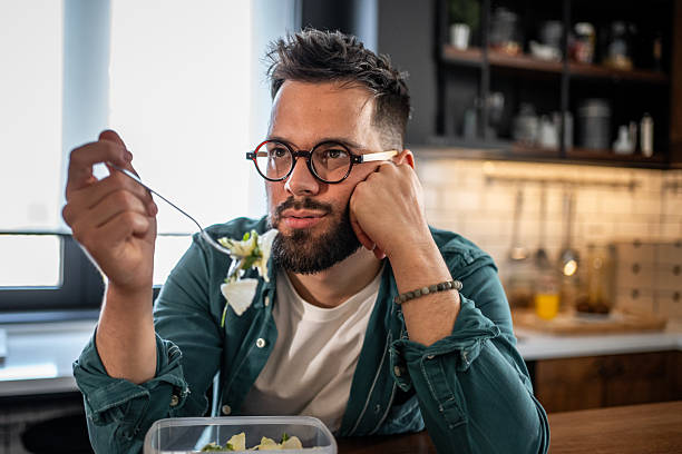 istock Bored young man reluctantly eating salad at home 2215526825