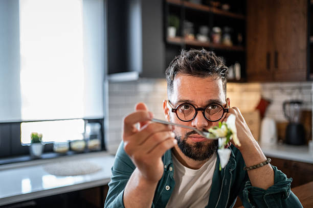 istock Bored man reluctantly eating salad in the kitchen 2215526829