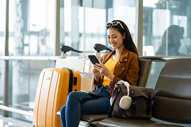 istock Young asian woman traveler using smartphone for checking flight information and playing social media app for shopping online while waiting with her luggage at the airport terminal. 2215526993