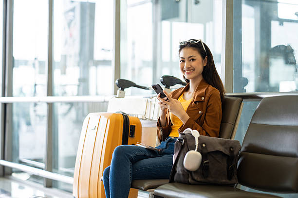istock Young asian woman traveler using smartphone for checking flight information and playing social media app for shopping online while waiting with her luggage at the airport terminal. 2215526999