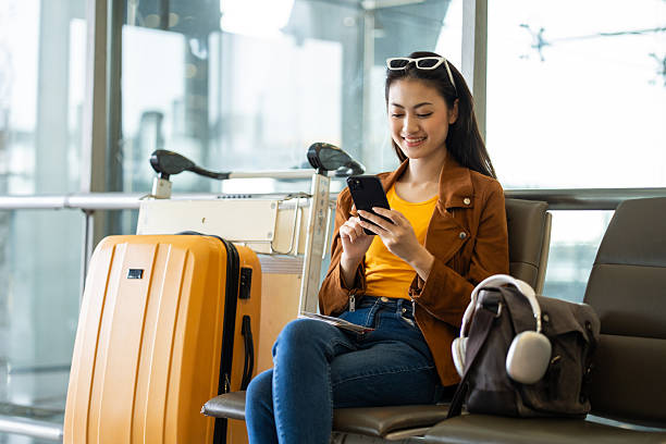 istock Young asian woman traveler using smartphone for checking flight information and playing social media app for shopping online while waiting with her luggage at the airport terminal. 2215527001