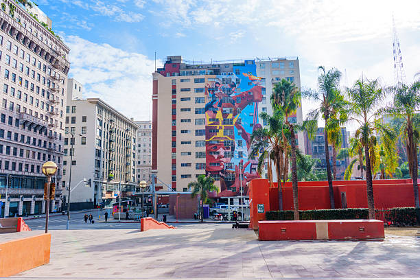 Los Angeles, California - December 3, 2024: Wide-angle view of a colorful mural on a building at Pershing Square Metro Station, showcasing urban art amidst palm trees under a bright blue sky.