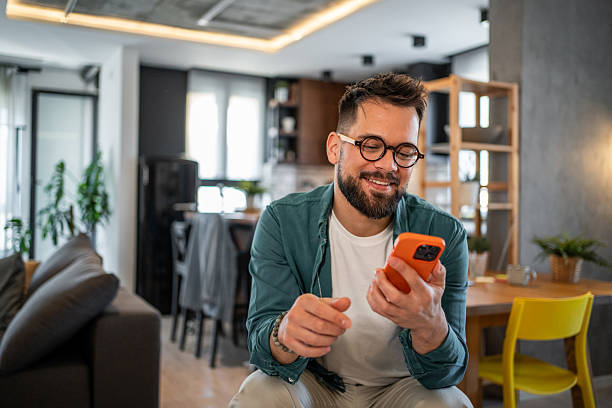istock Smiling young man using smartphone at home reading good news 2215528355
