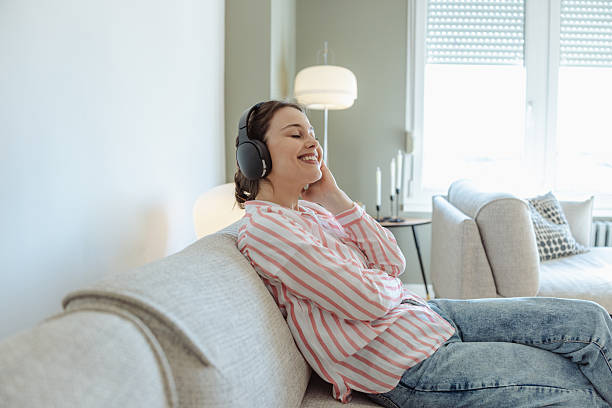 istock Young woman enjoying music on headphones while relaxing on a comfortable sofa 2215530708