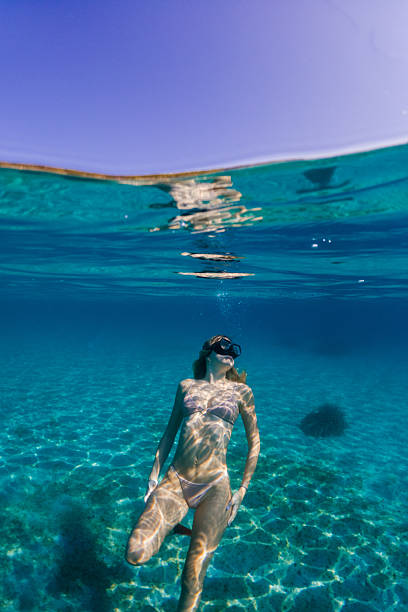 Beautiful woman relaxing and enjoying and playing underwater. She wears bikini and looks very attractive and graceful. Sunbeams coming from sea surface