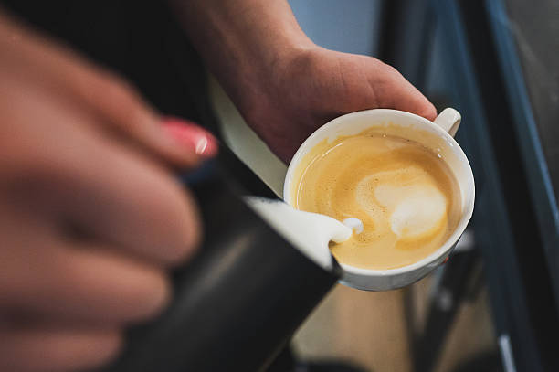 A barista skillfully pours steamed milk into espresso, creating intricate latte art. The close-up captures the precise motion of pouring, emphasizing the craftsmanship behind coffee preparation
