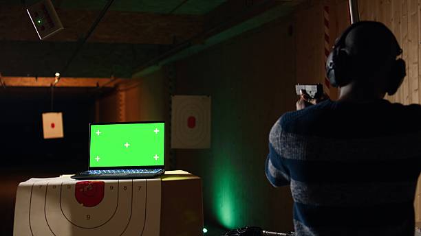 Green screen laptop next to man in firing range pressing mechanism to recall paper targets. Mockup notebook and person training with handguns on bullseye, sharpening skills, camera A