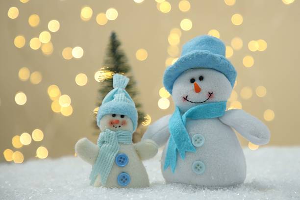 istock Cute decorative snowmen on artificial snow against blurred lights, closeup 2215548574
