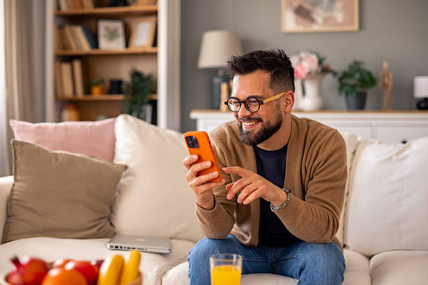 istock Smiling Man with Glasses Using Phone in Cozy Well-Lit Living Room 2215548613